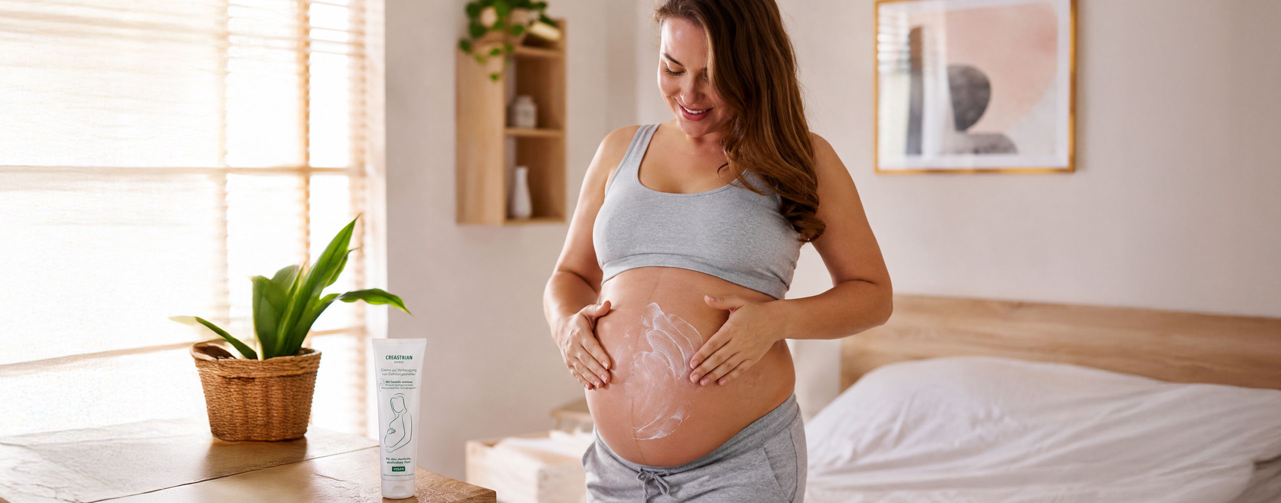 Schwangere Frau pflegt Babybauch mit Creme im Schlafzimmer -Creastrian Mama